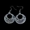 White circular earrings with intricate spiral and swirl cut-out designs, featuring a hypnotic pattern inside a round silhouette, hanging from silver hooks against a black background.