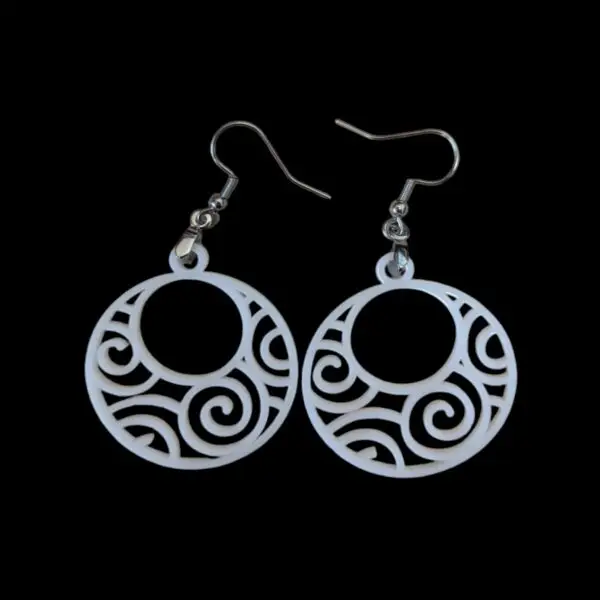 White circular earrings with intricate spiral and swirl cut-out designs, featuring a hypnotic pattern inside a round silhouette, hanging from silver hooks against a black background.