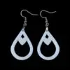 Close-up of sleek white teardrop-shaped dangle earrings featuring a diamond-shaped cut-out, suspended from silvertone surgical steel ear wires against a stark black background.