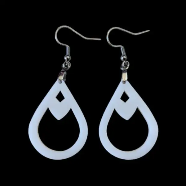 Close-up of sleek white teardrop-shaped dangle earrings featuring a diamond-shaped cut-out, suspended from silvertone surgical steel ear wires against a stark black background.