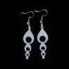 White dangle earrings featuring a vertical series of decreasing circular cutouts, creating a bubble chain effect, suspended from silver hooks on a black background.