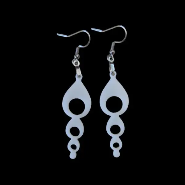 White dangle earrings featuring a vertical series of decreasing circular cutouts, creating a bubble chain effect, suspended from silver hooks on a black background.