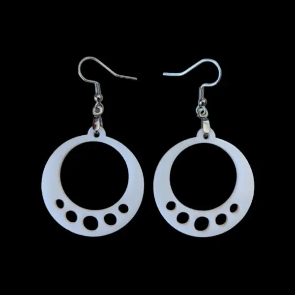 White laser-cut acrylic hoop earrings with five circular cutouts along the bottom edge, hanging from silver-tone hooks against a black background.