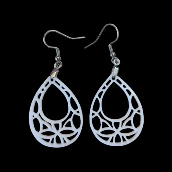 White geometric teardrop-shaped earrings with intricate cut-out design, featuring a web-like pattern inside a teardrop silhouette, hanging from silver hooks against a black background.