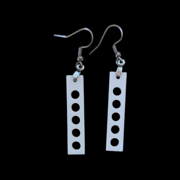 White rectangular earrings with five circular cutouts arranged vertically, hanging from silver hooks against a black background.