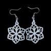 White geometric flower-shaped earrings with intricate cut-out design, hanging from silver hooks against a black background.