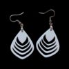 White teardrop-shaped earrings with a series of nested petal-like cutouts, creating a geometric floral effect, hanging from silver hooks against a black background.