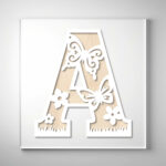 Laser-cut wooden letter "A" featuring butterflies, flowers, and grass cutout designs over a natural wood grain background.