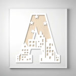 Laser-cut wooden letter "A" featuring a city skyline and starry night cutout design over a natural wood grain background.